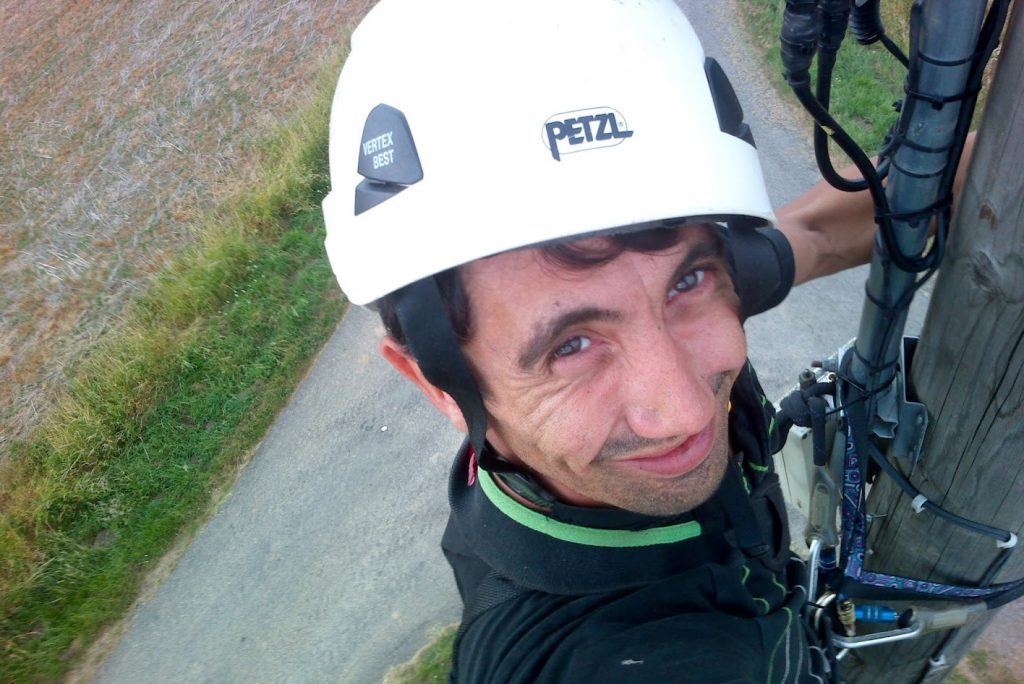 Technicien casqué et harnaché intervenant en hauteur sur poteau télécom bois