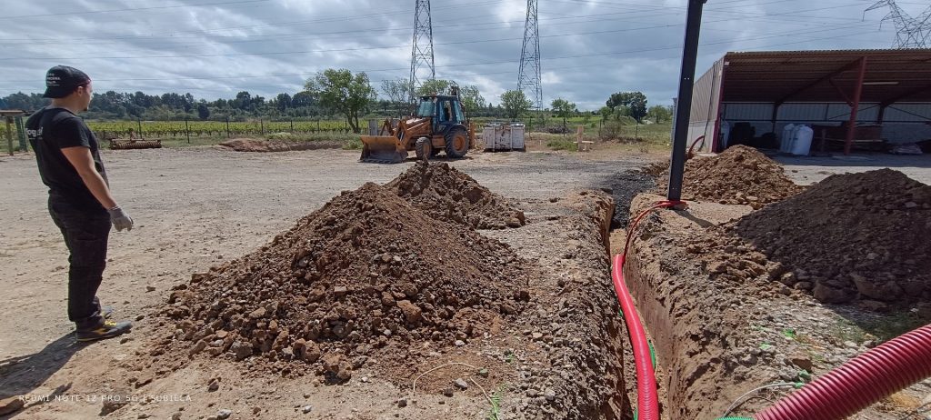 Tranchée avec fourreaux électriques rouges pour raccordement centrale photovoltaïque, tractopelle