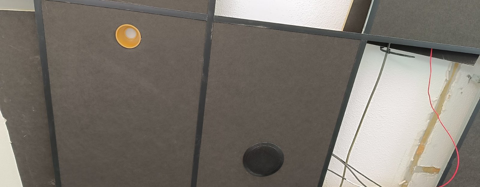 Installation en cours d'un haut-parleur encastré dans un faux-plafond, câblage apparent